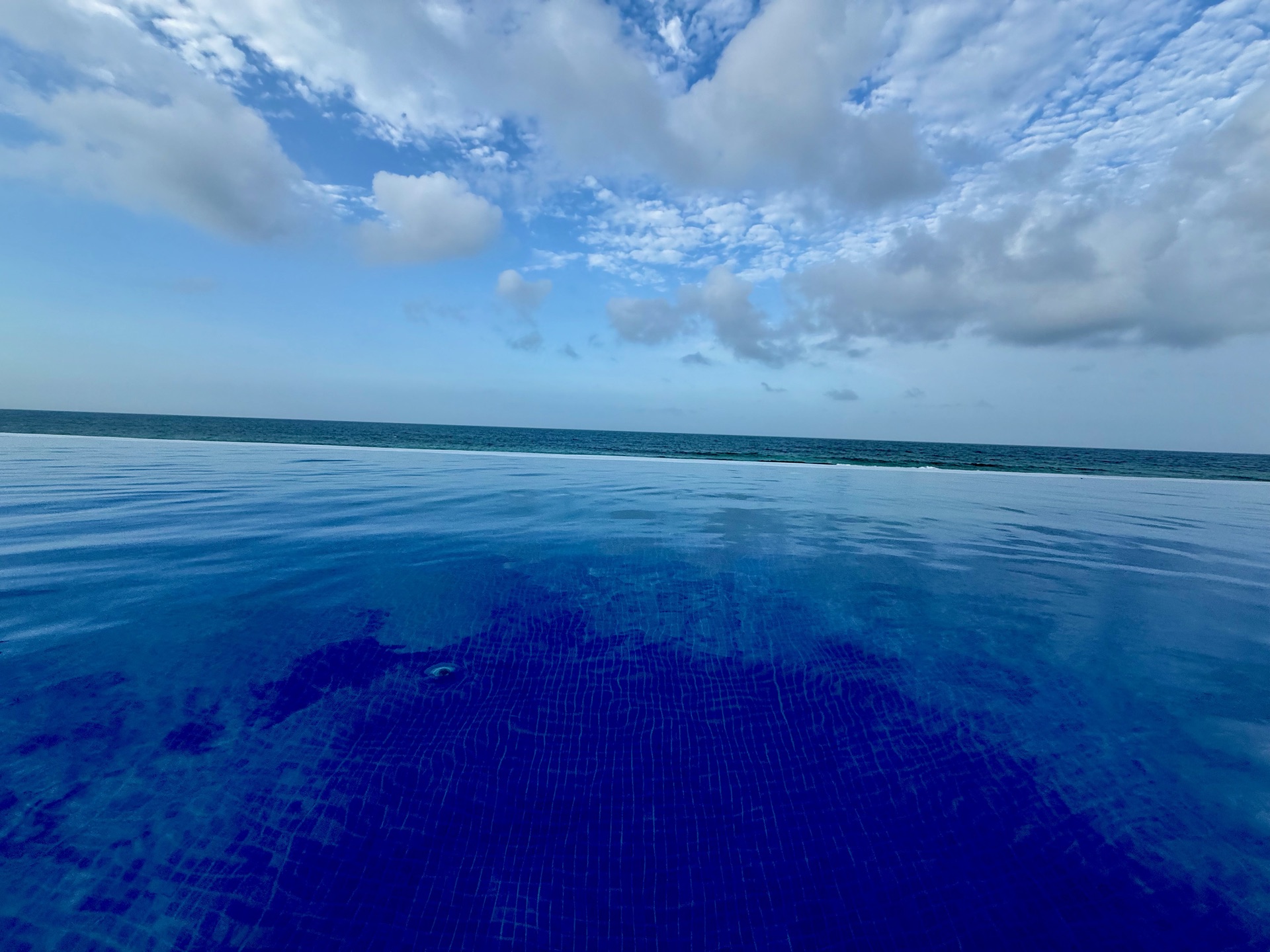 Close view of the teal infinity pool tile meeting the Caribbean Sea Isla Mujeres